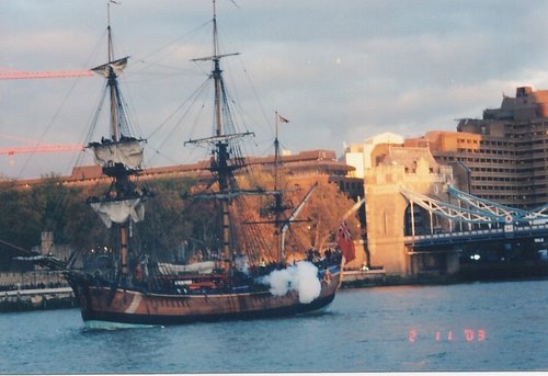 a view of sailing ship on the Thames, with cannons blasting at the Tower Bridge