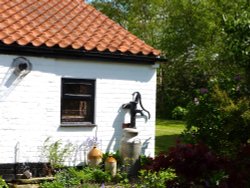 Old pump and milk churn on the side of a house in Belton Wallpaper