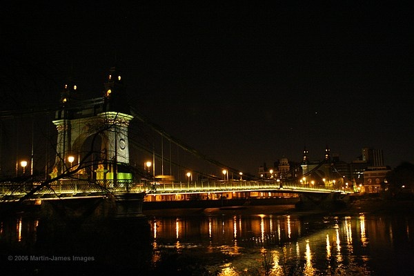 London Hammersmith Bridge at night from the towpath on the Barnes side of the River Thames.