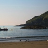 Early light on little Perhaver Beach, a fishing boat leaves neighboring Gorran Haven