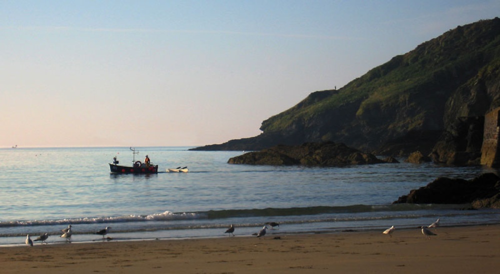 Early light on little Perhaver Beach, a fishing boat leaves neighboring Gorran Haven